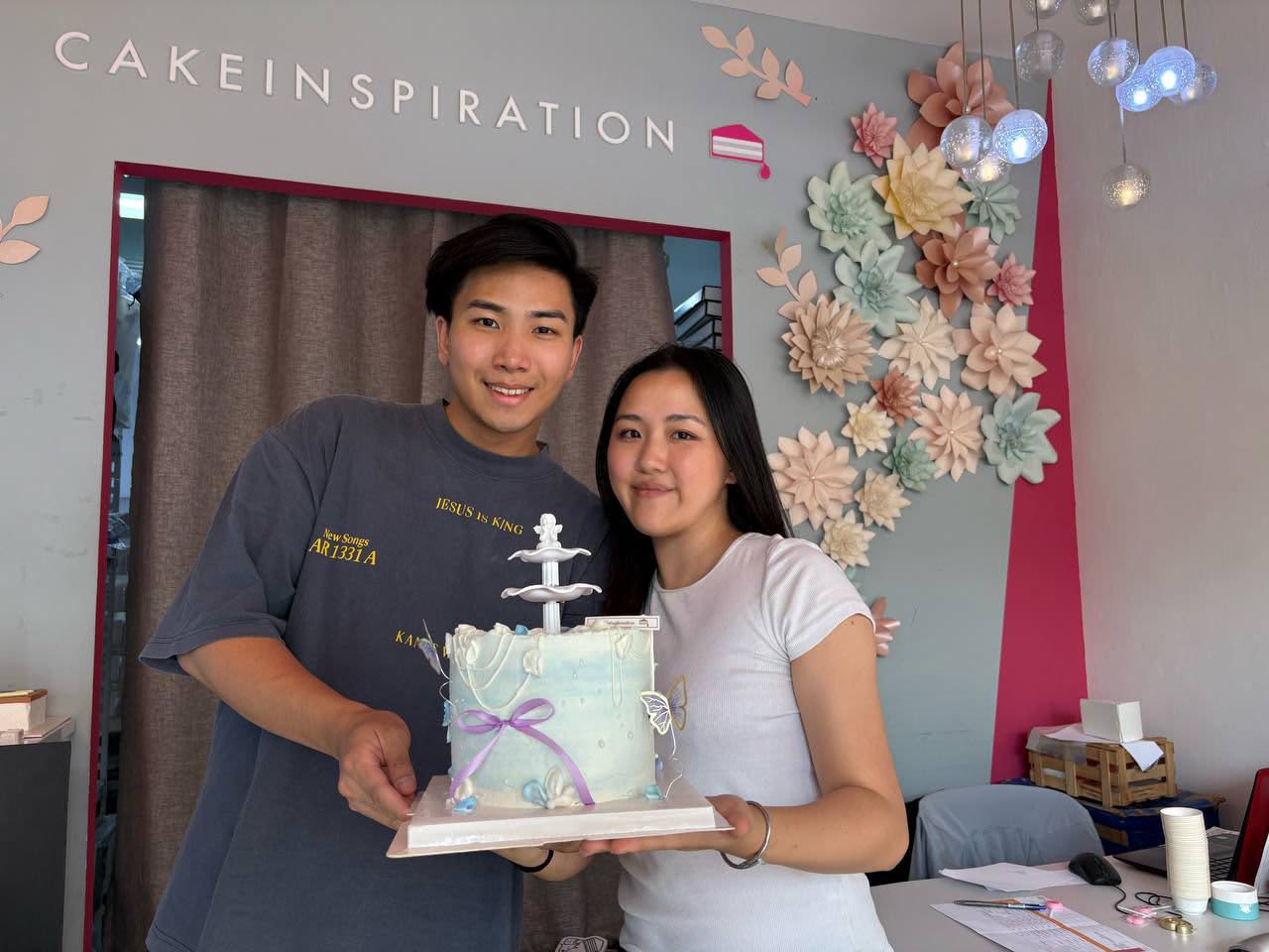 The founders of Cake Inspiration holding a custom cake at their Singapore storefront.